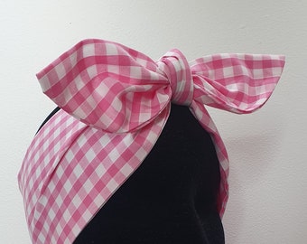 May include: Pink and white gingham headband with a bow tied on top. The headband is on a black mannequin head.