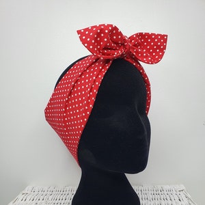 May include: A red fabric headband with white polka dots, styled with a bow, is displayed on a black mannequin head. The headband is a classic retro accessory. The white dots are evenly spaced on the red background, creating a vintage look.
