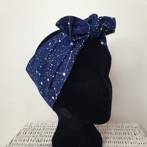 Könnte beinhalten: Ein marineblaues Stirnband mit einem weißen Sternenbildmuster und einer Schleife. Das Stirnband ist um einen schwarzen Mannequin-Kopf gebunden.