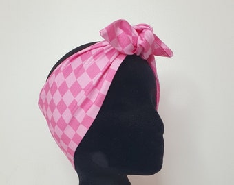 May include: Pink and white checkered headband with a bow on top. The headband is on a black mannequin head.