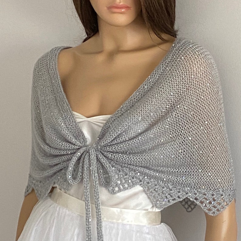 Tie front, light weight shawl. Knitted with fancy sequin yarn and triangle crocheted trim applied to the bottom edge of the shawl.
