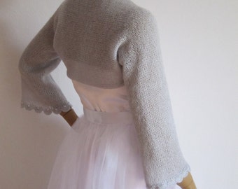 Könnte beinhalten: Eine hellgraue Strickjacke mit einem gewellten Saum. Die Jacke wird über einem weißen Tüllrock getragen.