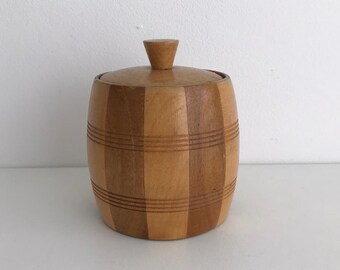 May include: A wooden barrel-shaped container with a lid. The container is made of light and dark wood and has a striped pattern.