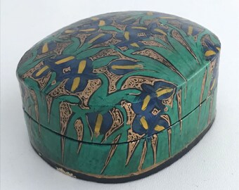 May include: A small, oval-shaped box with a green, blue, and gold floral design. The box is made of paper mache and has a black base.