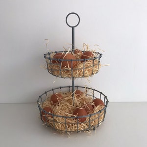 May include: A two-tiered wire egg holder with a grey finish. The holder is filled with brown eggs and straw.