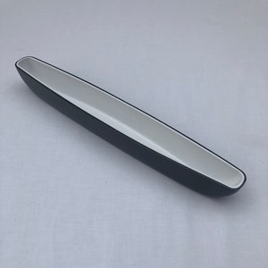 Op de afbeelding: Een zwarte keramische serveerschaal met een witte binnenkant. De schaal is lang en smal, met een afgeronde vorm.