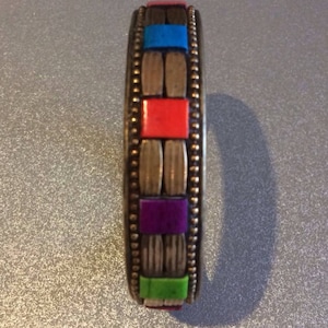 May include: A silver bangle bracelet with a decorative design of colorful squares. The squares are red, blue, green, and purple.