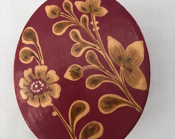 May include: An oval-shaped trinket box with a burgundy base and a floral design painted in gold and green.