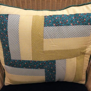 May include: A square cushion with a patchwork design. The cushion is made of yellow, green and white fabric with a floral pattern. The cushion has a green border.