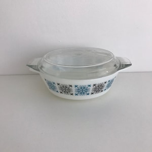 Puede incluir: Plato de horno blanco con tapa de vidrio. El plato tiene un patrón geométrico azul y marrón.