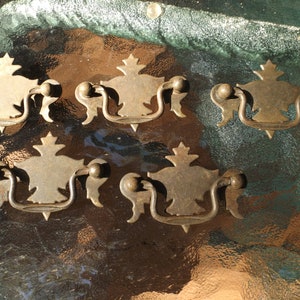 May include: Five antique brass drawer pulls with ornate designs. Each pull has a decorative top and a curved handle.