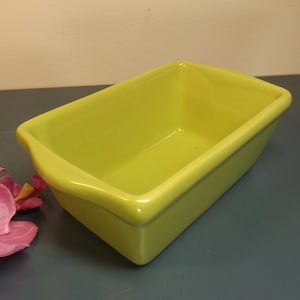 May include: A bright yellow ceramic loaf pan with a smooth, glossy finish. The pan is empty and ready for baking.