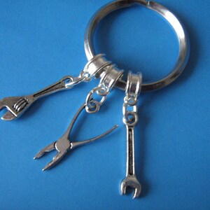 May include: Silver keyring with three charms: a wrench, a pair of pliers, and another wrench. The charms are attached to a silver key ring.