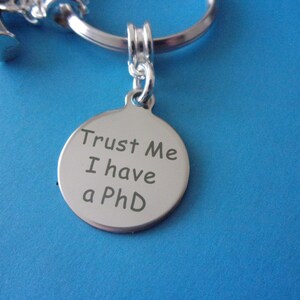 May include: Silver keychain with a round tag that says "Trust Me I have a PhD".