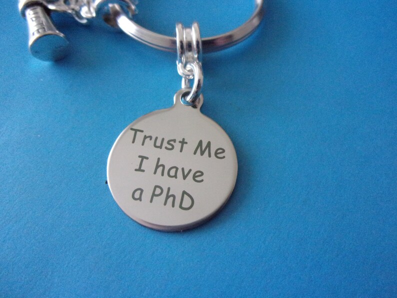 May include: Silver keychain with a round tag that says "Trust Me I have a PhD".