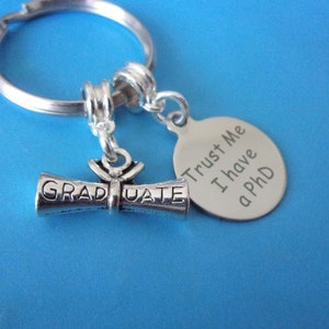 May include: Silver keychain with a graduation scroll charm and a round tag that says "Trust Me I have a PhD".