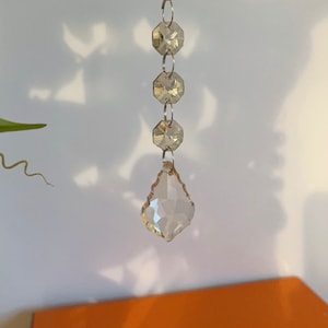 May include: A crystal chandelier prism with a teardrop shape and a faceted design. The prism is hanging from a silver chain.