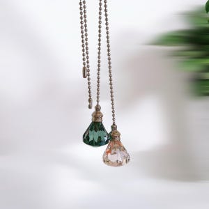 Könnte beinhalten: Drei dekorative Lichtschalterketten mit kristallförmigen Enden. Die Ketten sind silberfarben und die Kristalle sind grün und rosa.