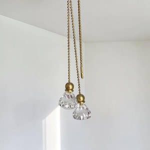 May include: Two ceiling fan pull chains featuring brass-toned ball chains and faceted clear crystal pendants. Each pendant is topped with a matching brass-toned metal cap, providing a decorative and functional extension for light or fan controls.