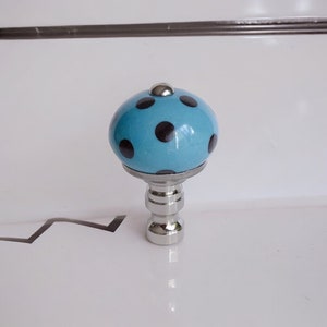 Op de afbeelding: Een blauwe keramische lampenkap met zwarte stippen en een zilveren metalen voet.