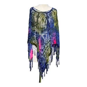 Peut inclure: Un poncho transparent à motifs dans les tons de bleu, vert et rose, avec un motif floral noir. Le poncho a un ourlet à franges et est présenté sur un mannequin. Le tissu semble être du velours.