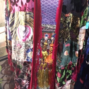 May include: A long, red velvet kimono with a patchwork design featuring various floral patterns and textures. The kimono has tassels and fringe details.