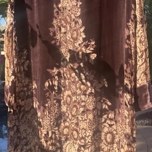 Peut inclure: Long manteau en velours marron foncé avec un motif floral marron clair. Le manteau a des manches longues et un col. Le motif floral est concentré au centre et sur les bords.