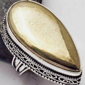 May include: A silver ring with a large, teardrop-shaped, gold-colored stone. The stone has a textured surface and is set in a decorative silver band with an ornate design. The ring is a statement piece of jewelry.