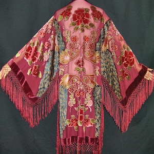 Peut inclure: Robe de style kimono bordeaux avec broderies florales et paon. La robe présente des manches longues avec des bordures à franges et des accents de velours. Le tissu transparent révèle le design complexe, créant une esthétique élégante et bohème.