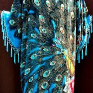Peut inclure: Longue robe fluide ornée d'un motif de plumes de paon dans les tons bleu et turquoise, avec des détails dorés. Le vêtement est orné de franges sur les manches et l'ourlet. Le motif de plumes de paon est orné de sequins.