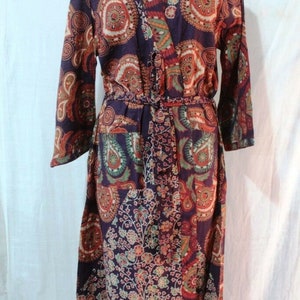 Peut inclure: Une longue robe violette à imprimé paisley. La robe a une ceinture à nouer et des manches longues.