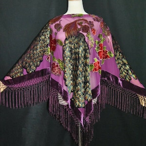 Peut inclure: Un châle en soie violet avec un motif de paon et une bordure à franges. Le châle est sur un mannequin.