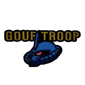 May include: A blue and gold embroidered patch with the text "GOUF TROOP" and a cartoon image of a blue robot head.