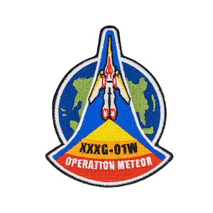 May include: A blue, yellow, red, and white embroidered patch with a spaceship flying over a green and blue globe. The text "XXXG-OTW OPERATION METEOR" is written in black on the patch.