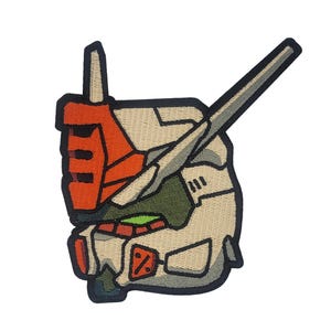 May include: Embroidered patch featuring a cartoon-style robot head with a white, gray, and orange color scheme. The robot head has a large, pointed antenna and a single, large eye.
