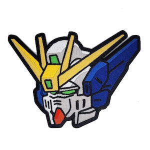 May include: Embroidered patch featuring a detailed illustration of a robot head with a yellow, blue, and gray color scheme. The robot has a large, pointed head with a yellow antenna and a blue wing on the side.