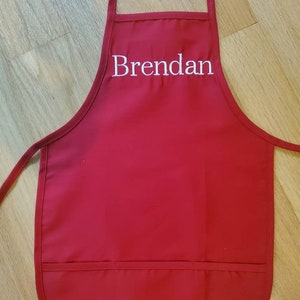 May include: Red apron with a large pocket and the name "Brendan" embroidered in white on the front.