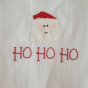 May include: White fabric with a red embroidered Santa Claus face and the text "HO HO HO" in red.