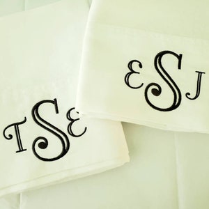 May include: Two white pillowcases with embroidered black initials. One pillowcase displays the initials "TSE", and the other shows "ESJ". The letters are in a decorative, elegant font, adding a personalized touch to the bedding.