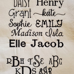 May include: A white fabric with black embroidered names, including Amelia, Brooke, Daisy, Henry, Grant, Kate, Sophie, Emily, Madison, Isla, Elle, and Jacob. The fabric also has black embroidered letters, including R, B, H, T, S, E, A, B, G, K, D, S, &, J, R, A, W, I, O, G, A, C, M, and L.