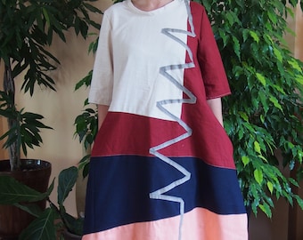 May include: A long, multi-colored dress with a geometric design. The dress is made of a soft, lightweight fabric and has a relaxed fit. The dress is white, red, navy blue, and pink.