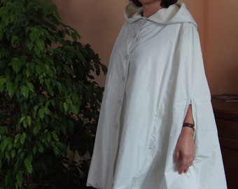 May include: A white hooded cape with a button fastening and long sleeves. The cape is made from a lightweight fabric and has a relaxed fit.