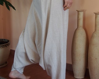 May include: A woman wearing a pair of white linen pants with a wide, white waistband. The pants are loose-fitting and have a flowing, draped look. The woman is standing on a tiled floor with three decorative vases behind her.
