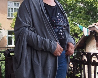 May include: A long, gray cardigan with long sleeves and a draped design. The cardigan is worn over a black t-shirt with a sparkly design and blue jeans.
