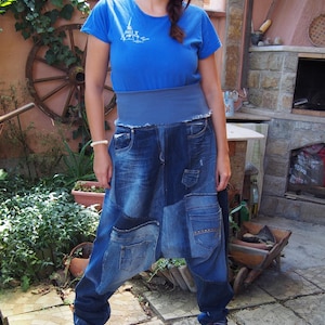 Può includere: Una donna indossa una maglietta blu con un disegno della Torre Eiffel, un'ampia fascia blu in vita e pantaloni di jeans patchwork. I pantaloni hanno più tasche e un design unico. Indossa scarpe da ginnastica bordeaux.