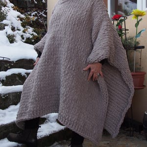 May include: A taupe-coloured chunky knit poncho with a high turtleneck. The poncho has a loose, flowing design, ideal for layering. The thick knit fabric provides warmth and a cosy feel. This versatile outerwear piece is perfect for autumn and winter. The poncho is a versatile outerwear piece.