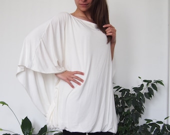 May include: A white, loose-fitting, long-sleeved top with a gathered hem. The top is made of a soft, stretchy fabric and has a relaxed fit. The model is wearing black leggings.