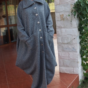 May include: A long, grey, oversized coat with a large collar and a button fastening. The coat has a loose, flowing fit and is made of a soft, textured fabric.