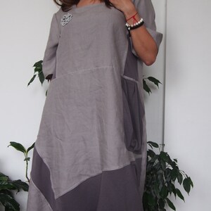 May include: A gray linen dress with a patchwork design. The dress has a scoop neck and short sleeves. It features a decorative flower brooch on the left side of the chest.