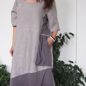 May include: A gray linen dress with a purple and gray patchwork design. The dress has a scoop neck, short sleeves, and a loose fit. It features a patch pocket on the left side.